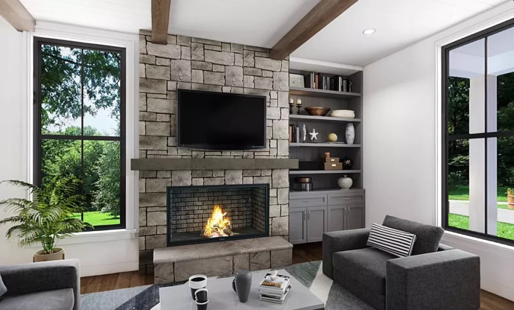 open concept great room with stone fireplace, wood beams, built-in shelving, and large windows in modern farmhouse house plan