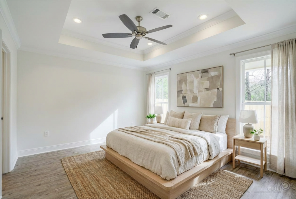 modern farmhouse primary bedroom with tray ceiling, large windows, neutral tones, and wood bed frame