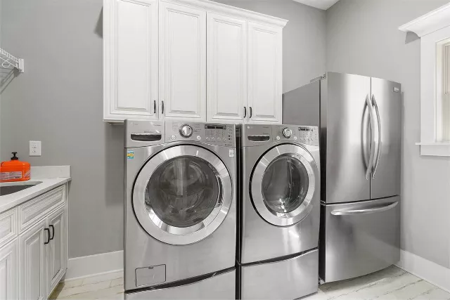 Classic cottage laundry room features a white and gray granite countertop  positioned over a sil…
